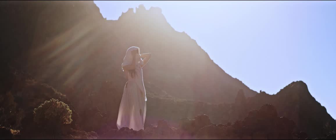 Woman in a white dress against a dramatic sunset and a mountain in the background