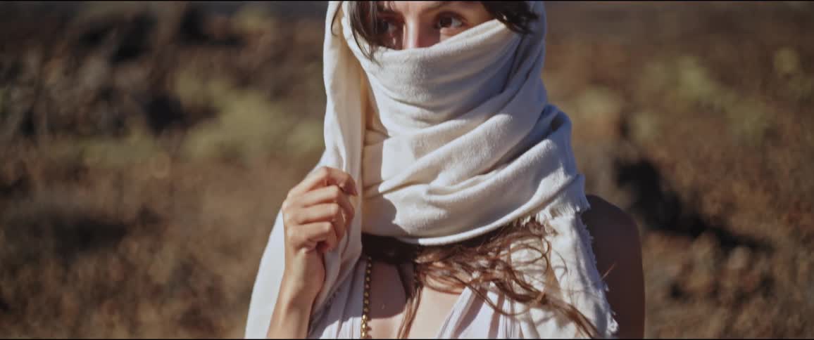 Young woman with a white scarf covering her face while in a desert and mountainous environment