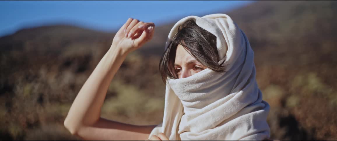 Woman with a scarf covering her face while in a natural environment with mountains around her