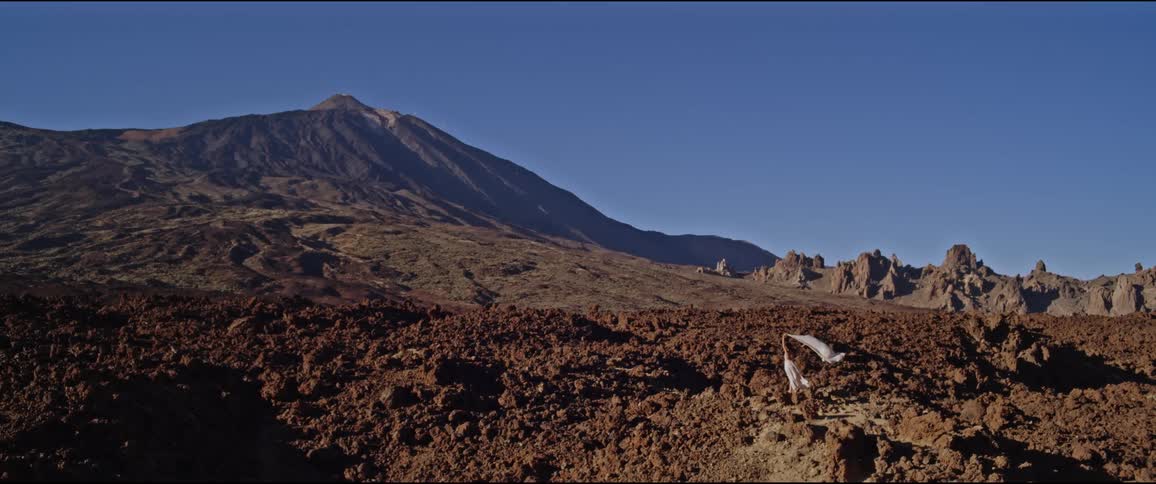 Woman holds white fabric up to in the wind as she faces the mountain