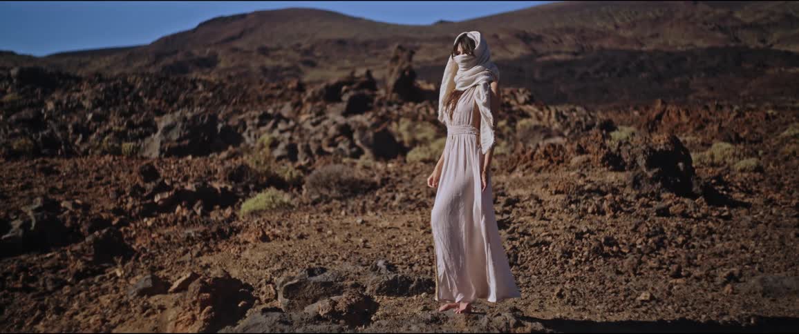 Woman dressed in light clothes and a headscarf standing in a barren terrain with rocks