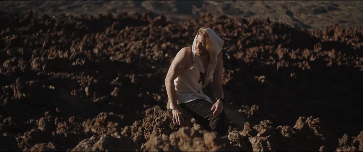 Man with hoodie sitting on rocks in natural environment