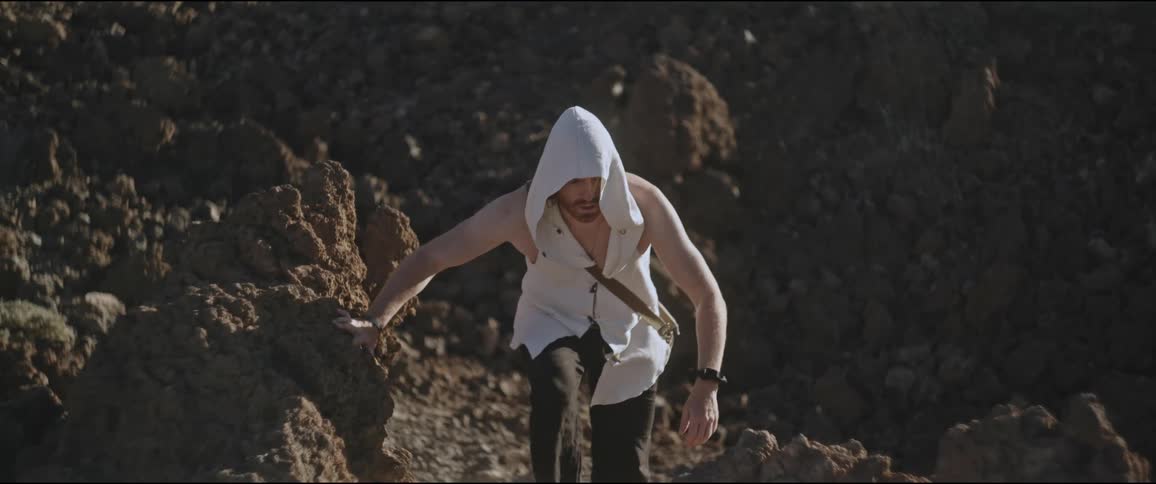 Man wearing a sleeveless coat with a hood climbing rocks in a natural environment