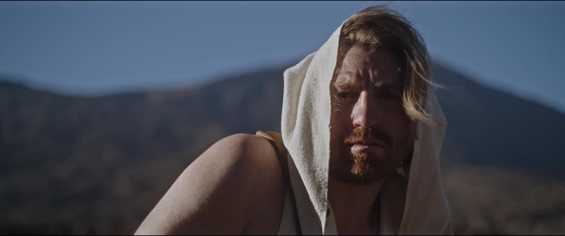 A man wearing a headscarf looks into the distance in a nature