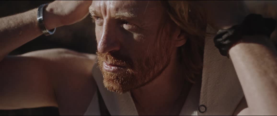 Close up of the face of a bearded man with long hair taking off a hood in nature