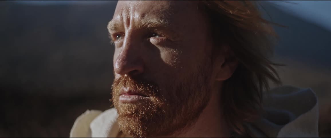 Close up of the face of a bearded man with long hair taking off a hood in nature
