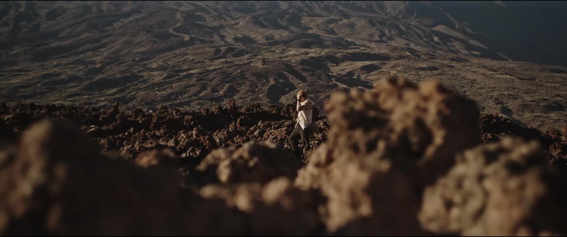 Person taking the hood off their head and contemplating a mountainous and rocky landscape