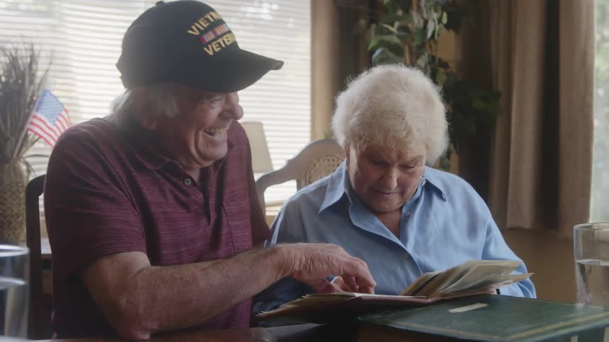 A husband and wife are talking and laughing while looking at a photo album
