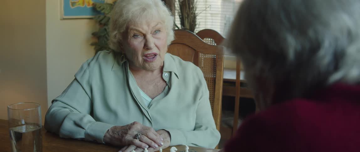 An elderly woman and a two man are sitting at a table talking and happy
