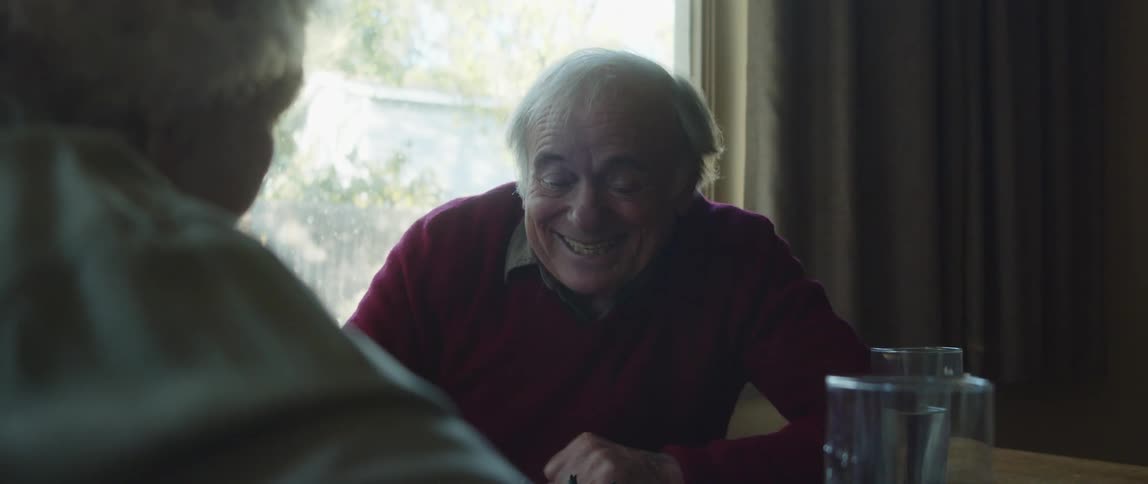 A happy elderly couple talking to each other while playing chess at home