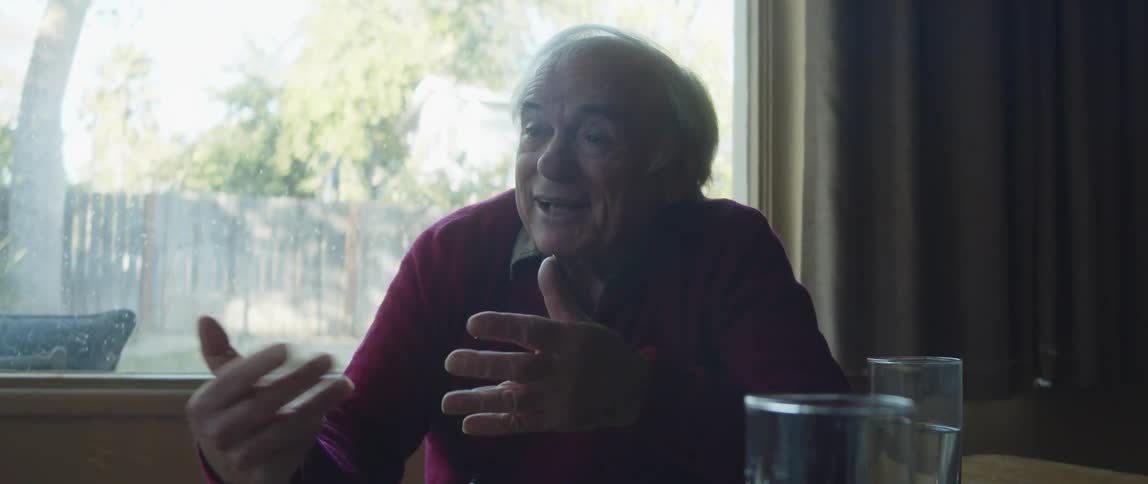 An elderly man smiles and laughs while having a conversation at home