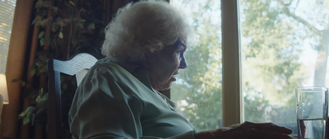 Elderly lady sitting at the table talking raising her hands up