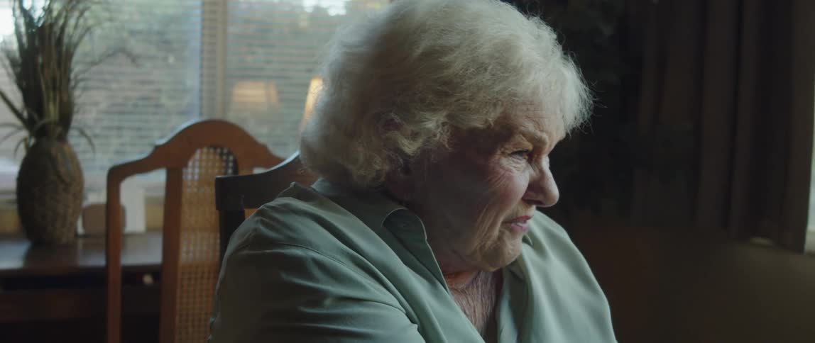 An elderly woman is sitting in a chair and talking to someone in front of her