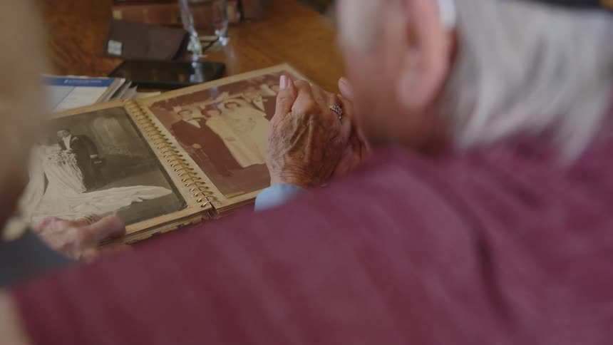 An elderly couple looks at a wedding photo while holding hands