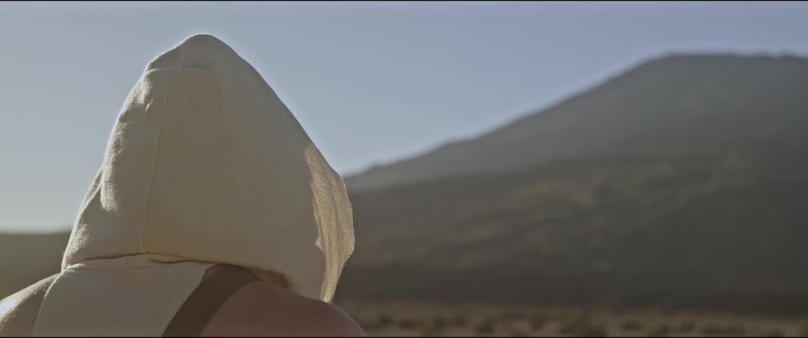 Back view of a man with a white hoodie in an environment surrounded by mountains