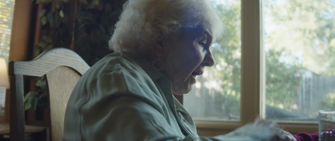 An elderly woman sits at a table talking to another person