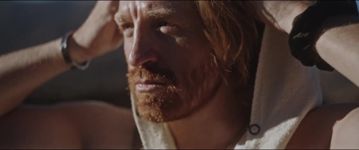 Close up of the face of a bearded man with long hair taking off a hood in nature