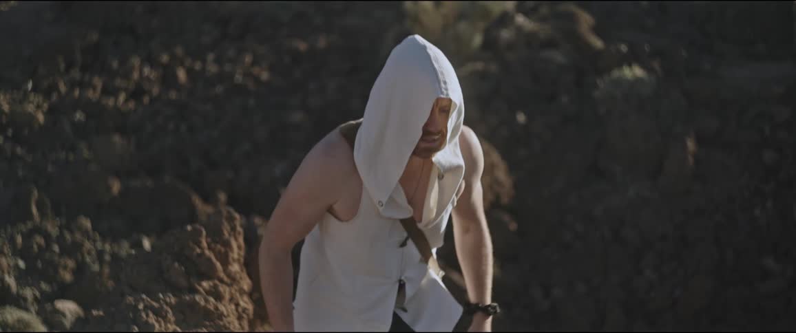 A man in a tunic and head covering walking through rocky terrain