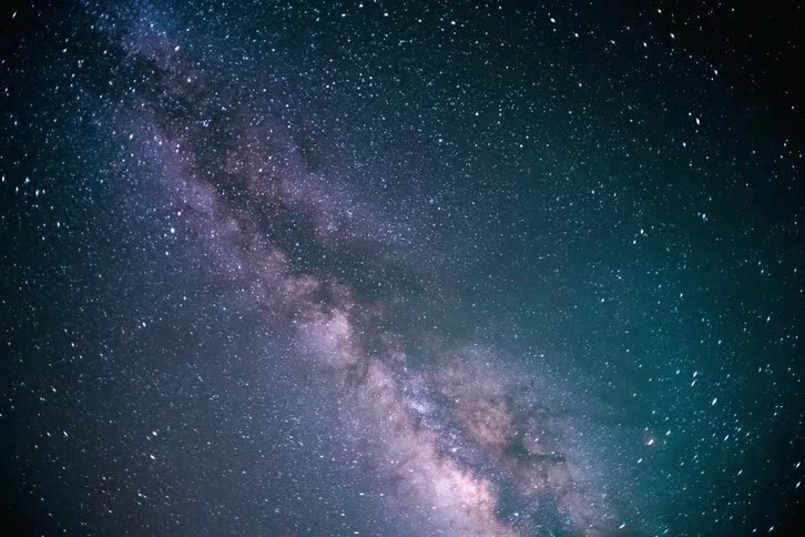 A view of dark and starry space with a large nebula and several shooting stars passing by and it is getting daytime