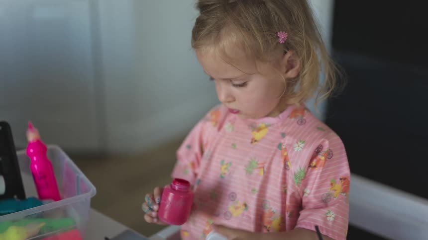 A girl in a pink colorful outfit paints with watercolors using her fingers