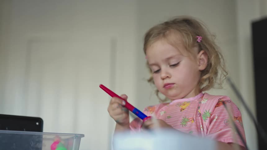 A girl wearing a pink colorful shirt painting with watercolors at home
