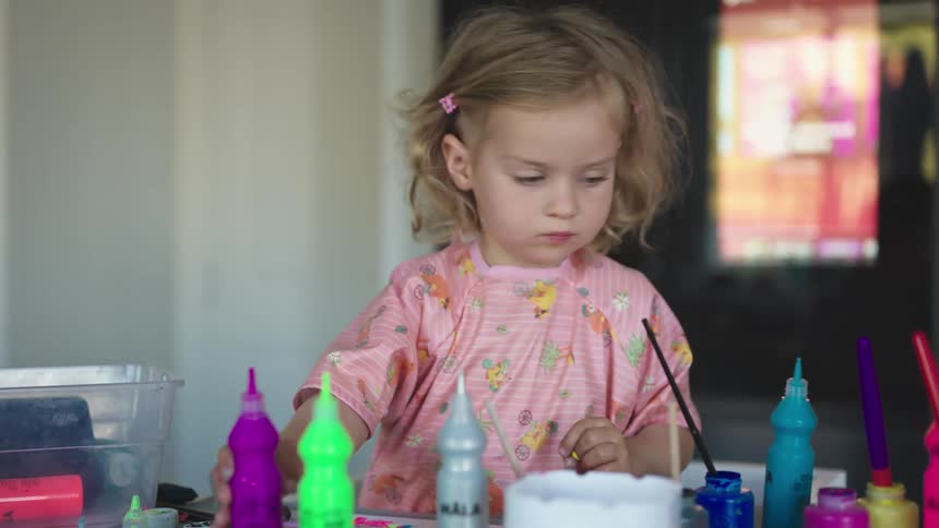 A young girl moves a bottle of paint around on a table
