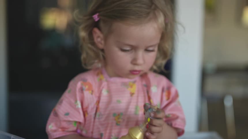 Little girl taking a tube of paint and squeezing it onto a canvas