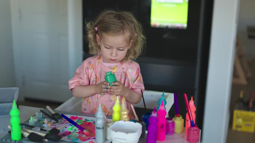 A girl wearing a pink colorful shirt painting with watercolors at home