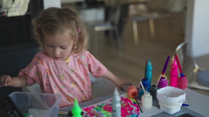 Little girl playing with paint tubes on the table