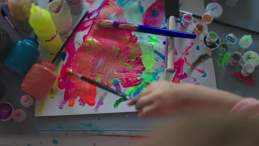 Childs hand painting a paper with a brush with paint