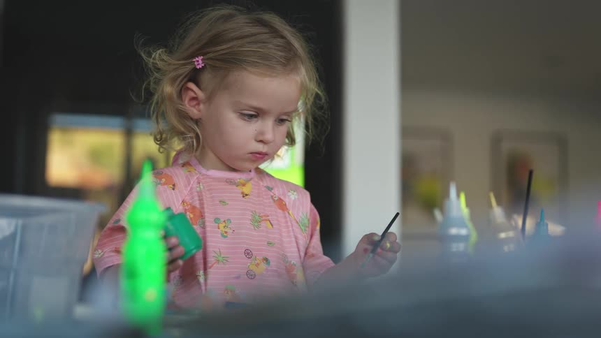 Little blonde girl playing with a brush and paints