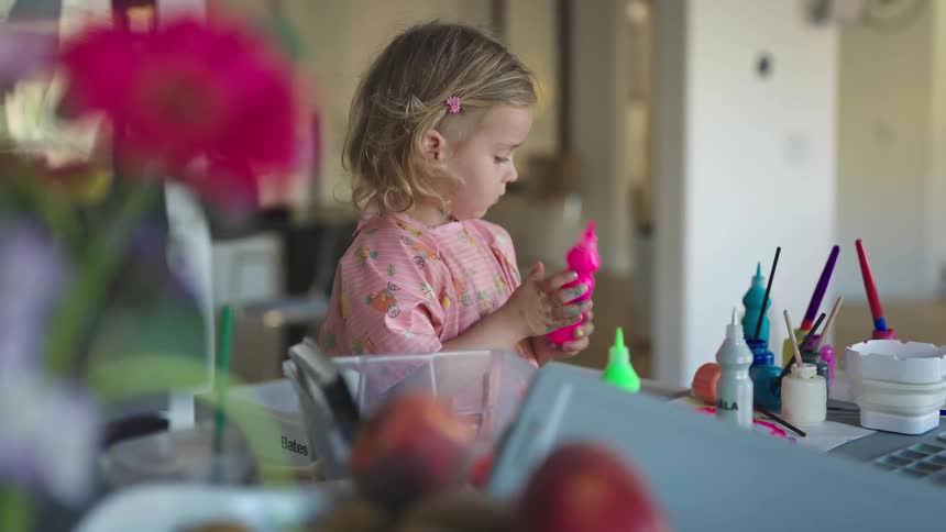 Little girl squeezes pink paint onto paper on the table in front of her