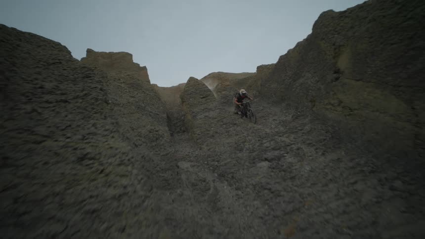 A person riding a bicycle down a narrow dirt trail between tall steep rock formations