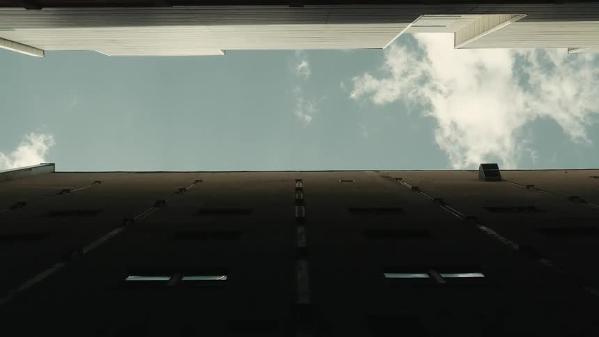 Looking up an alley with two buildings on the sides and a partly cloudy sky