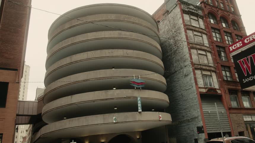 A multilevel spiral parking garage with a rounded design between traditional brick buildings in the city