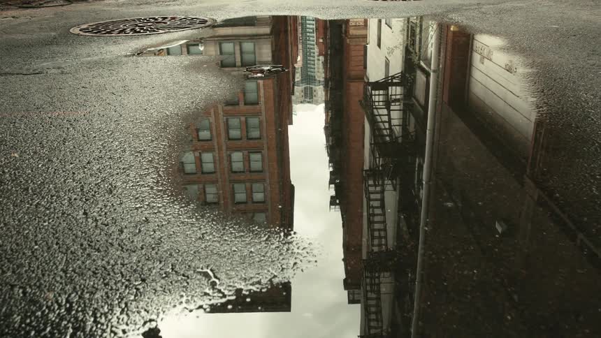 Tall city apartment buildings reflected in a pool of water on a street
