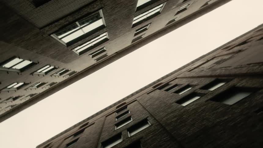 Upward angle view between two tall buildings with multiple windows and a symmetrical appearance under a cloudy sky