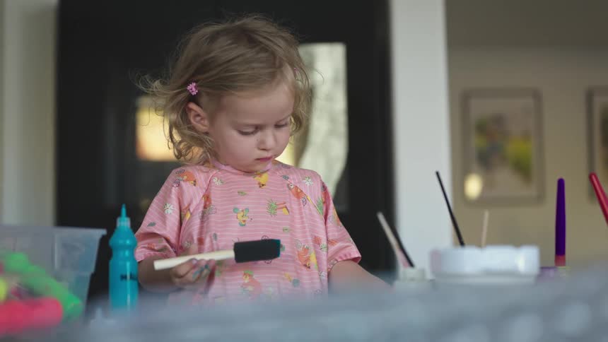 Little blonde girl holding a spatula with paint