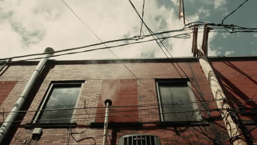 A brick building with two windows and tangled wires in front with a small chimney spewing white smoke