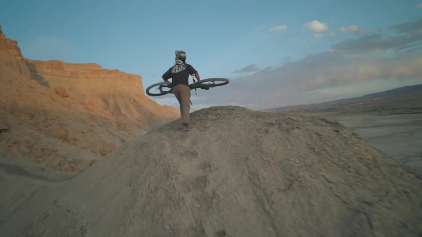 Man carrying a bicycle in his hands to the top of a mountain