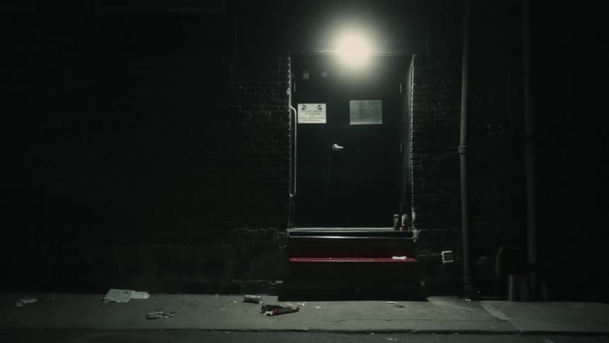 A single bulb lights the darkened stoop of a building in the middle of the night