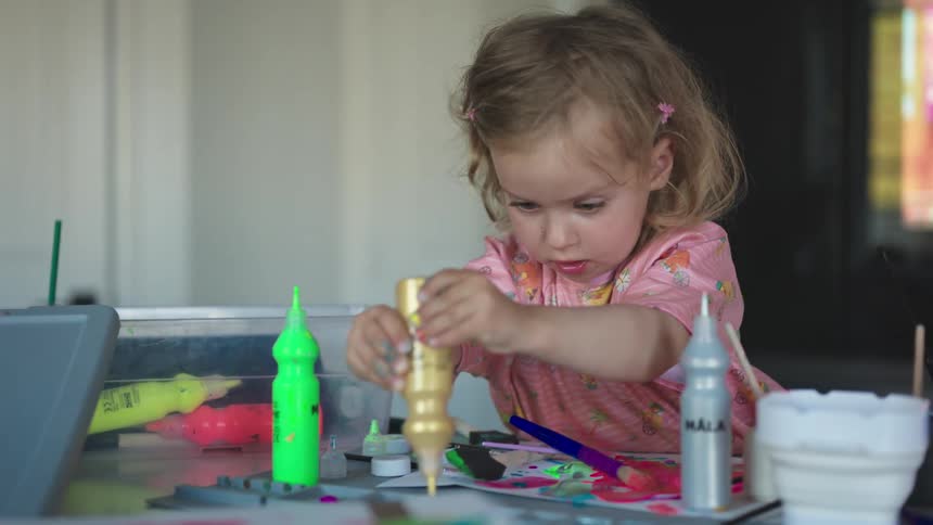 Little girl playing with paint tubes
