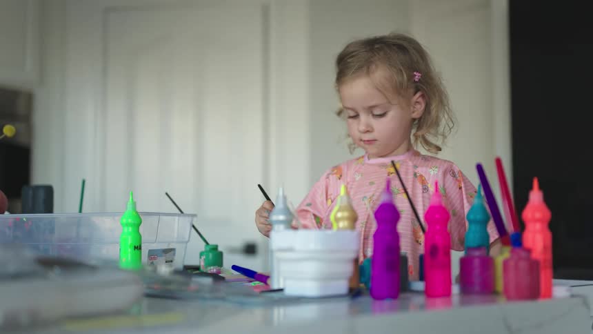 Little girl at a table playing paint with gouache paint