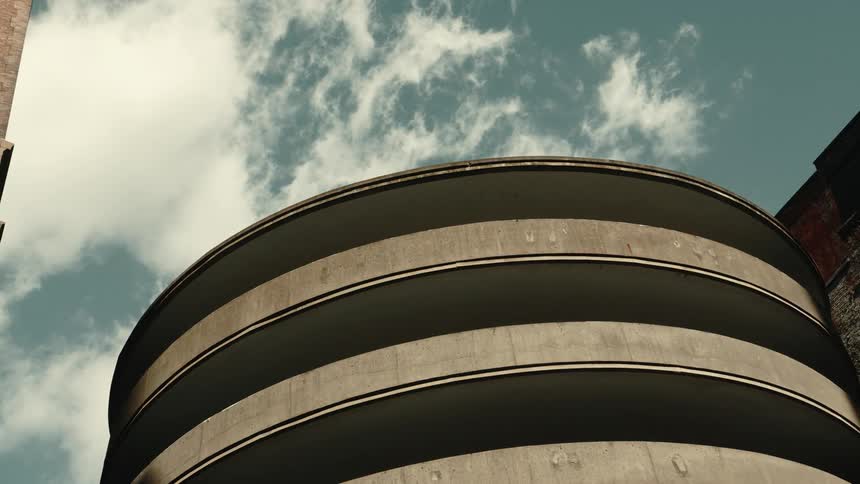 Clouds pass over circular parking garage standing next to a commercial building