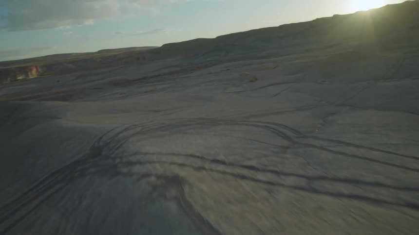 Aerial view of a barren desert landscape with small hills and slopes at sunset