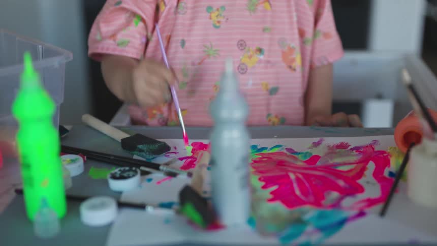 A young girl in pink jabs a paint brush against a piece of paper