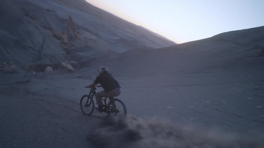 A person riding a bicycle down a narrow dirt trail in the desert mountains