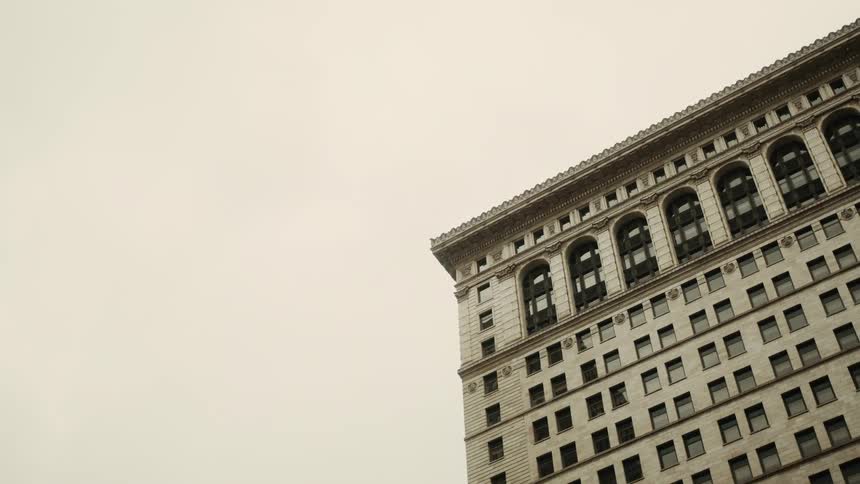 Bird flying in front of a white brick building on a cloudy day
