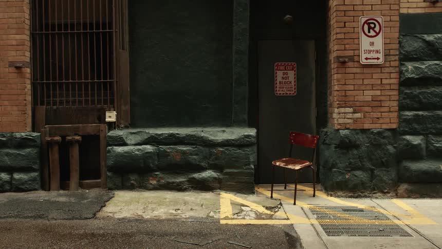 Red chair sits on sidewalk near an exterior door with a do not block sign
