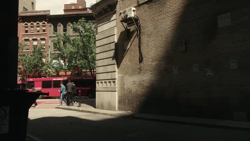 Person walks out of shadowed alley toward a busy street passing by residential buildings